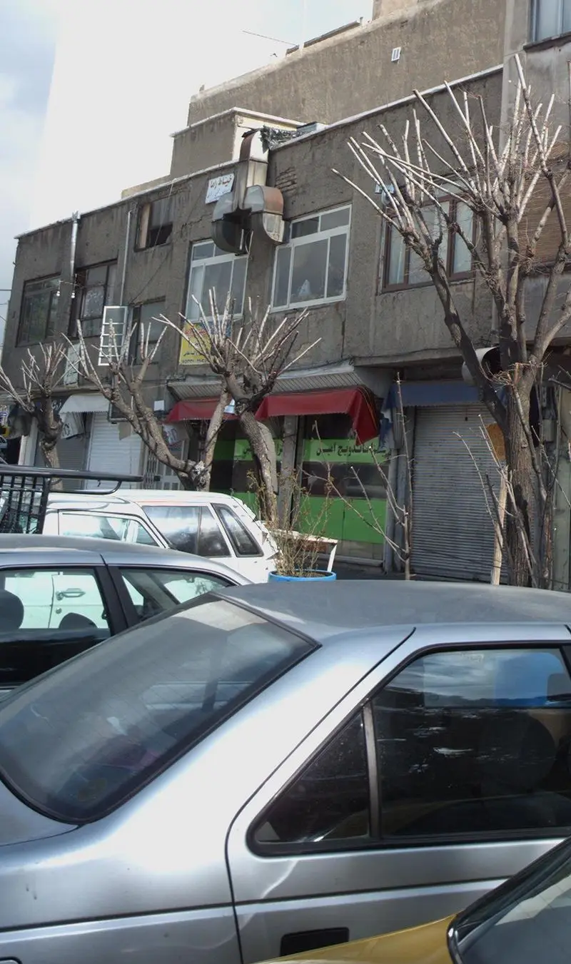 نمای بیرونی فست فود پیتزا و ساندویچ امین در خیابان با ساختمان‌های اطراف، خودروهای پارک شده و درختان خشک.