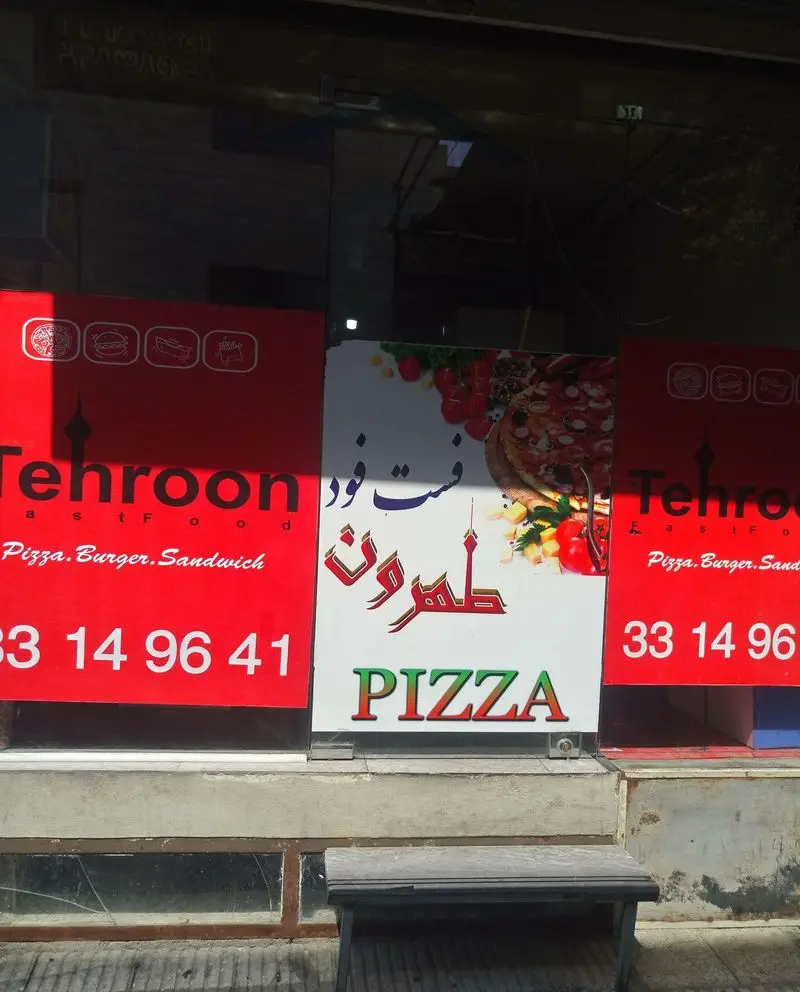 تصویر تابلوی فست فود طهرون شامل لوگو، پیتزا، برگر، ساندویچ و شماره تلفن ۳۳۱۴۹۶۴۱ برای سفارشات در تهران.