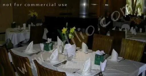 میز شام شیک و آماده در رستوران البرز با رومیزی سفید، دستمال‌های تاشده، گلدان گل زرد و جعبه دستمال سبز. فضایی دلنشین برای پذیرایی.