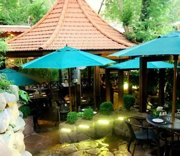 کافی شاپ اس پی یو: محیطی آرام و دلنشین در فضای باز با چترهای آبی، میز و صندلی‌های راحت و معماری سنتی.