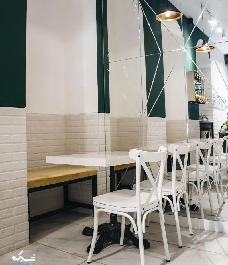 دکوراسیون داخلی کافه لایت با دیوارهای سفید و سبز، آینه‌های دکوراتیو هندسی، میز و صندلی‌های سفید شیک و فضای دلنشین و مدرن برای مشتریان.