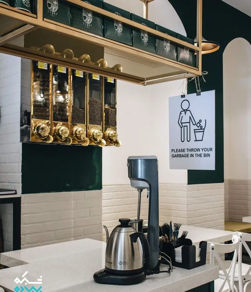 نمای داخلی کافه لایت با مخازن دانه قهوه تازه، طراحی مدرن و تجهیزات کامل آماده سازی قهوه. محیطی دلپذیر برای مشتریان.