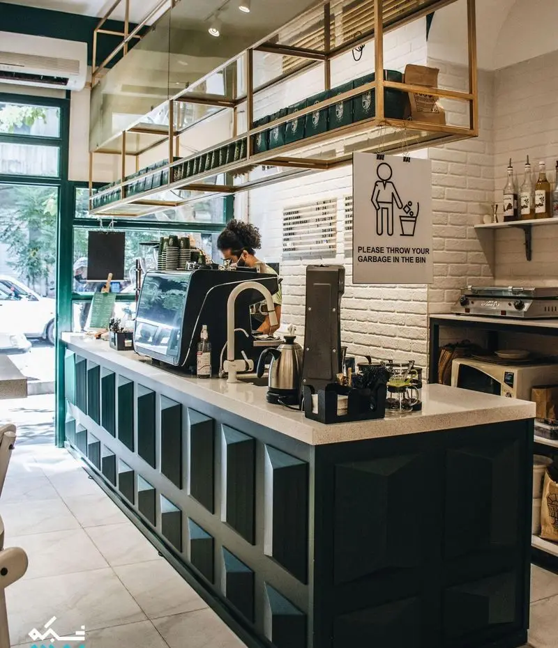 کافه لایت: فضای داخلی روشن و مدرن با پیشخوان شیک، باریستا حرفه‌ای و دستگاه‌های پیشرفته قهوه. قفسه‌های سقفی با بسته‌های قهوه.