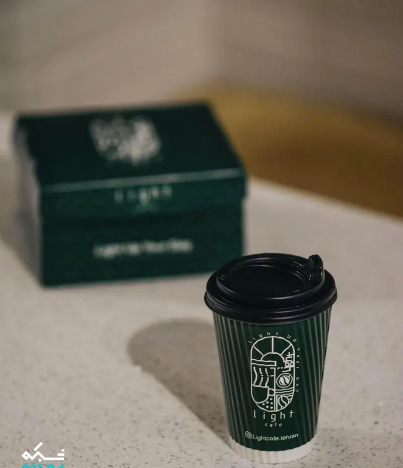 فنجان قهوه دلیوری کافه لایت با طراحی جذاب و لوگوی "Light up your day" و بسته بندی سبز شیک کافه لایت تهران.