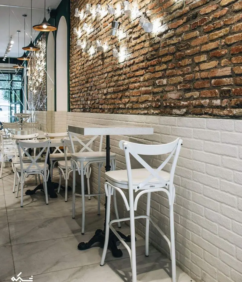 دکوراسیون داخلی کافه لایت با دیوار آجری، میزهای بار سفید و صندلی‌های صلیبی، نورپردازی خاص و فضایی مدرن و دلنشین.