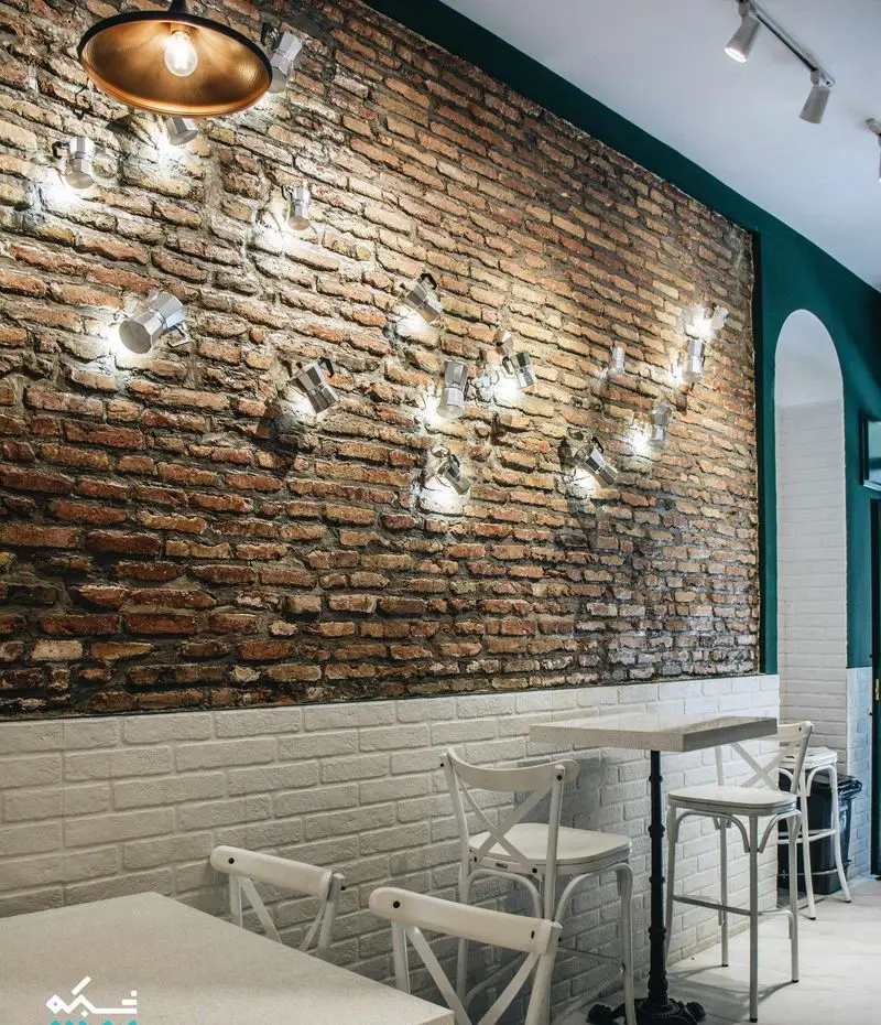 دکوراسیون داخلی چشم‌نواز کافه لایت: دیوار آجری با نورپردازی منحصر به فرد از موکاپات‌های درخشان و میز و صندلی‌های سفید شیک.