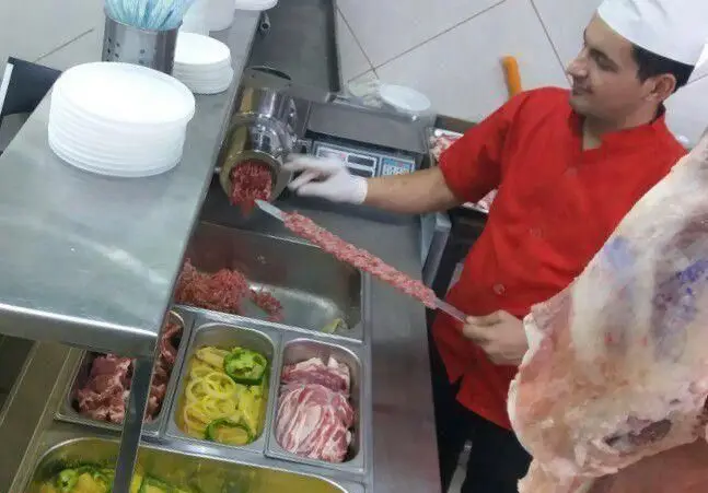 کباب‌پز کبابخانه اصیل گلپایگانی در حال آماده‌سازی کباب کوبیده تازه با گوشت چرخ‌کرده و سیخ کردن آن. محیط قصابی و رستوران سنتی.