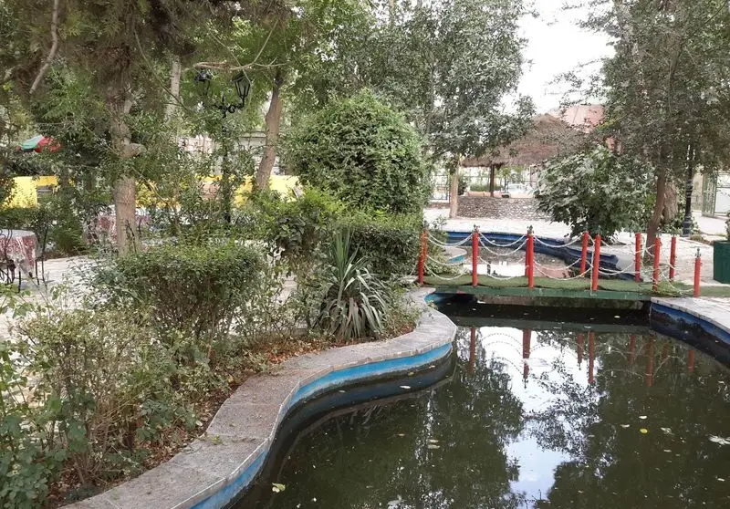 فضای دلپذیر باغ رستوران اشراق با حوض آب، پل کوچک تزئینی و درختان سرسبز، محیطی آرام برای تجربه غذایی لذت‌بخش.