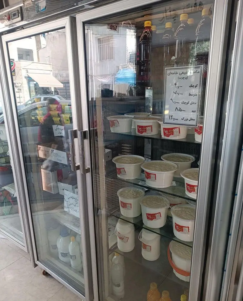 یخچال ویترینی لبنیات سنتی هفت چنار، پر از ماست طبیعی خامه ای ایرجرب در اندازه‌های گوناگون و بطری‌های شیر و دوغ، با لیست قیمت روی درب.