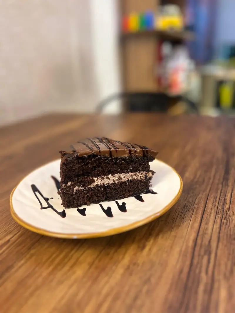 برشی کیک شکلاتی غنی و خوشمزه از کافه پارس، با فیلینگ کرم و سس شکلات، ایده‌آل برای لذت بردن در محیط دلنشین کافه.