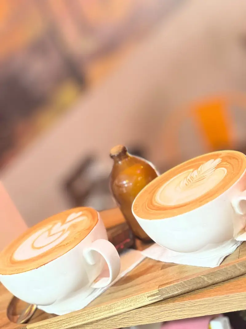 دو فنجان لاته داغ با لاته آرت زیبا روی سینی چوبی در فضای دلنشین کافه پارس. بهترین قهوه و نوشیدنی‌های گرم را در کافه ما تجربه کنید.