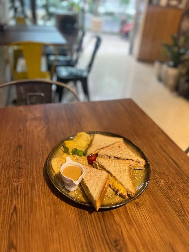 نمایی از یک بشقاب ساندویچ خوشمزه و تازه همراه با سس مخصوص، روی میز چوبی کافه پارس. ایده‌آل برای صبحانه یا میان‌وعده.