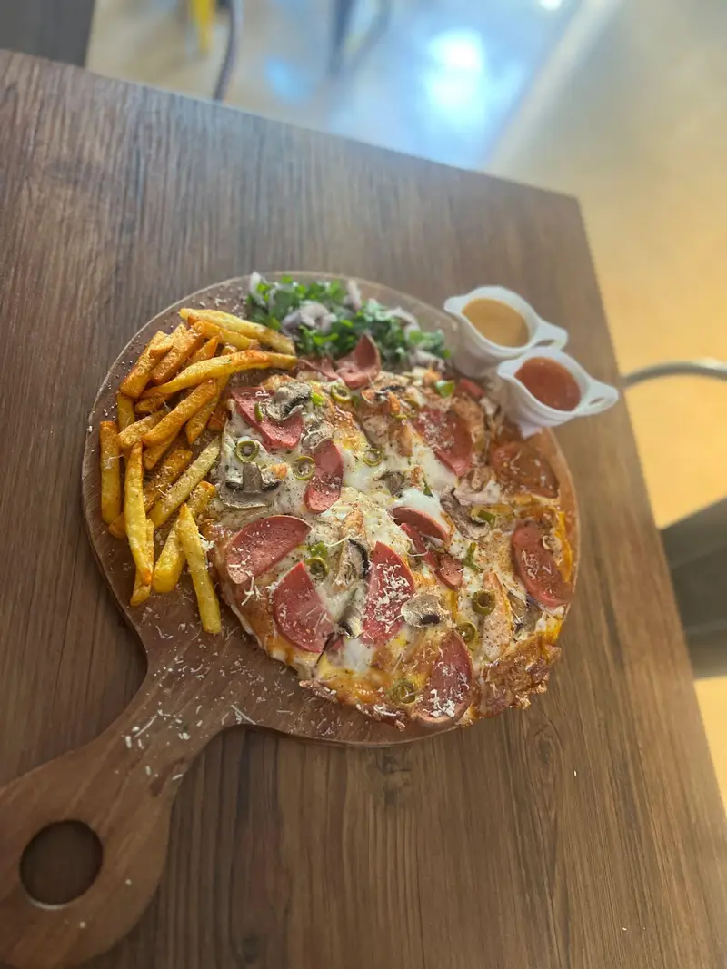 پیتزا خوشمزه کافه پارس با سوسیس، قارچ و زیتون در کنار سیب‌زمینی سرخ کرده و سس روی میز چوبی. غذای عالی برای کافه پارس.