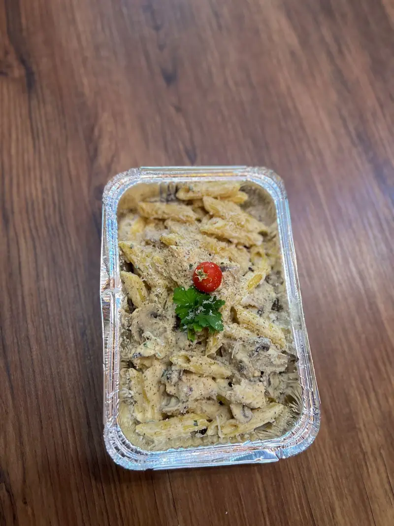 پاستا پنه خامه‌ای و قارچ کافه پارس در ظرف آلومینیومی، غذایی لذیذ و دلپذیر برای بیرون‌بر، با تزیین گوجه و جعفری.