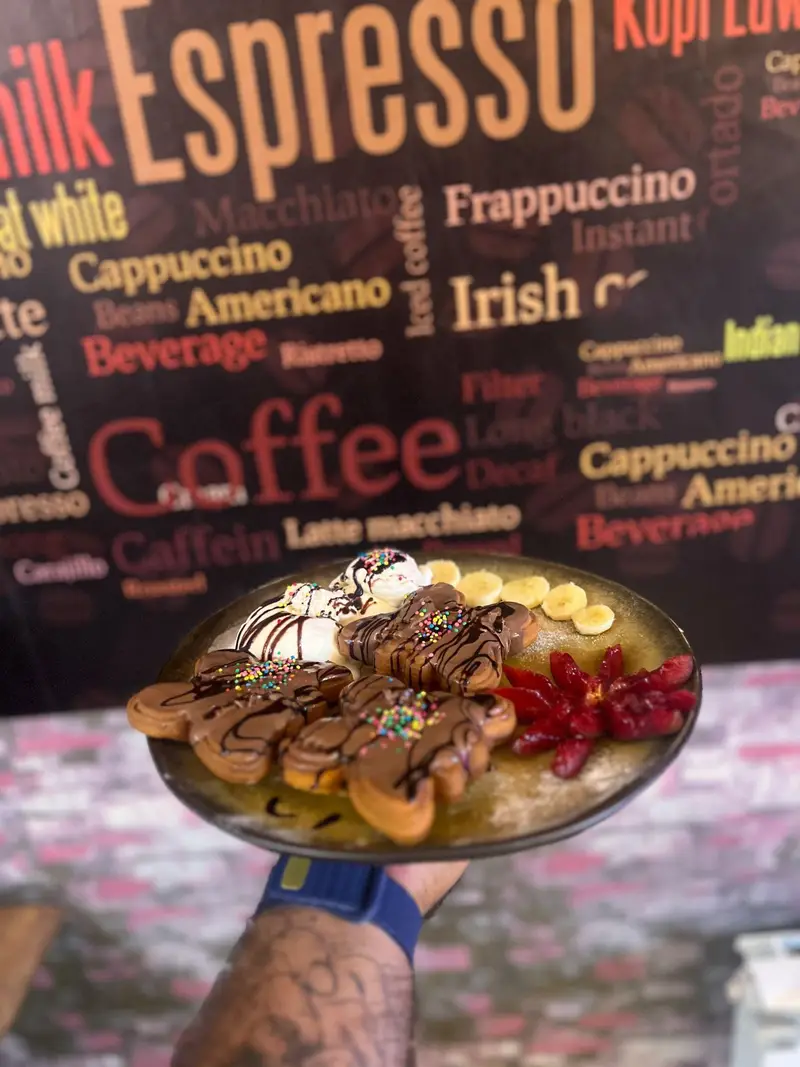 دسر وافل و بستنی لذیذ کافه پارس با سس شکلات، اسپرینکلز، موز و میوه در پس زمینه منوی قهوه و نوشیدنی.