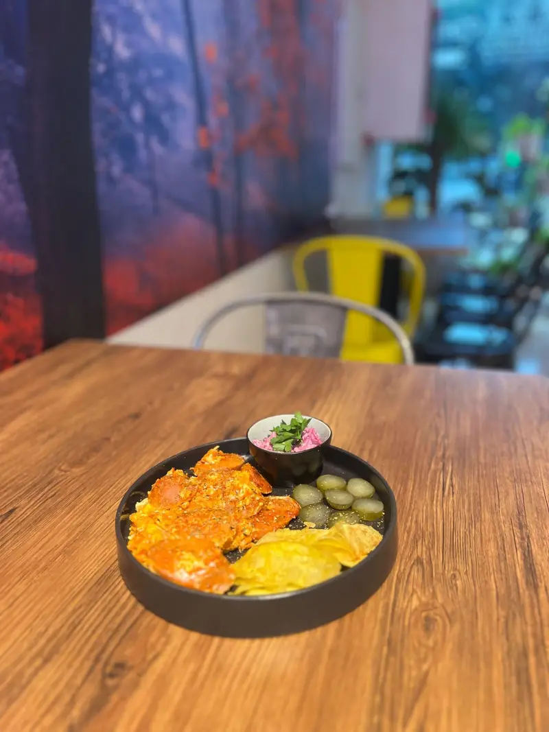 غذایی خوشمزه از تخم‌مرغ یا املت، چیپس ترد، ترشی خیار و دیپ مخصوص سرو شده روی میز چوبی در کافه پارس. تجربه طعم بی‌نظیر.