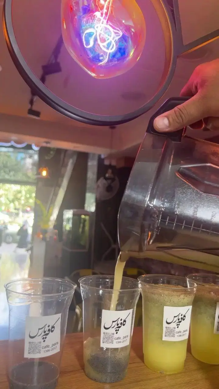 تصویری از تهیه و سرو نوشیدنی‌های تازه و خنک در کافه پارس: ریختن آبمیوه به لیوان‌های حاوی تخم شربتی برای مشتریان کافه پارس.