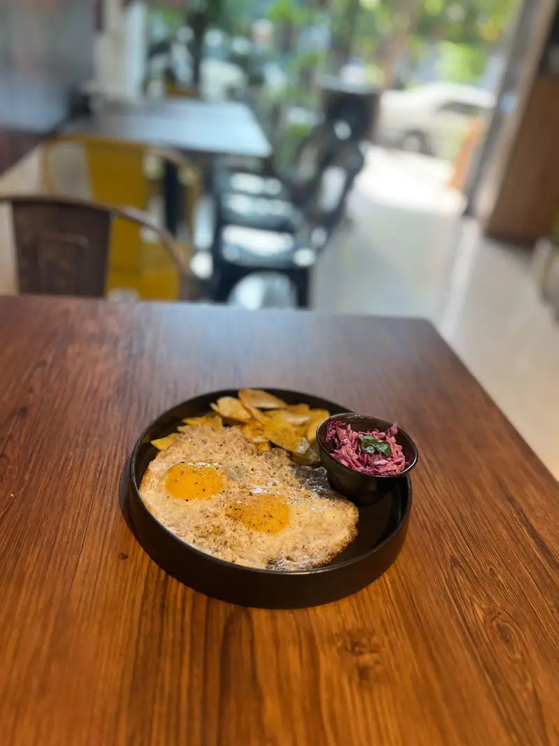 صبحانه اشتهاآور کافه پارس: دو تخم مرغ نیمرو با فلفل، برش‌های طلایی سیب‌زمینی و سالاد کلم بنفش تازه، روی میز چوبی با فضای روشن کافه.