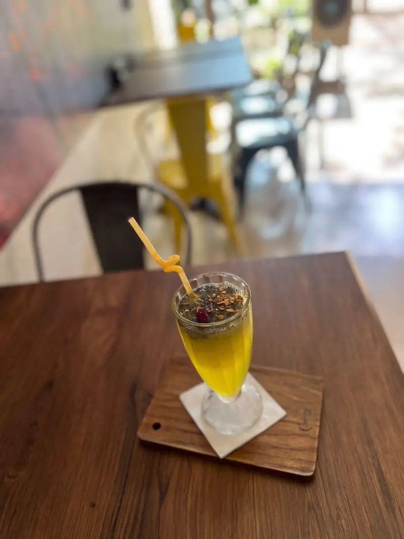 نوشیدنی خنک و خوشمزه در کافه پارس: اسموتی انبه با تاپینگ بذر چیا و گل محمدی در فضای دلنشین و دنج کافه پارس.