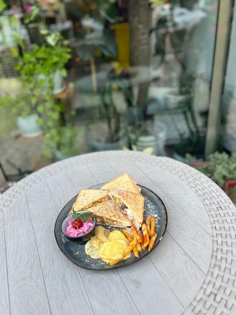 ساندویچ کلاب خوشمزه کافه پارس با سیب‌زمینی سرخ‌کرده و چیپس ترد روی میز بیرونی کافه، انتخابی عالی برای وعده شما.