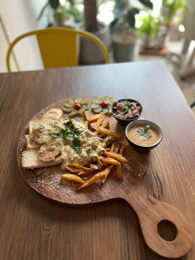 غذای محبوب کافه پارس: بشقاب چوبی با خوراک مرغ و قارچ در سس خامه ای، سیب زمینی سرخ کرده، سالاد کلم و ترشی تزیینی زیبا.