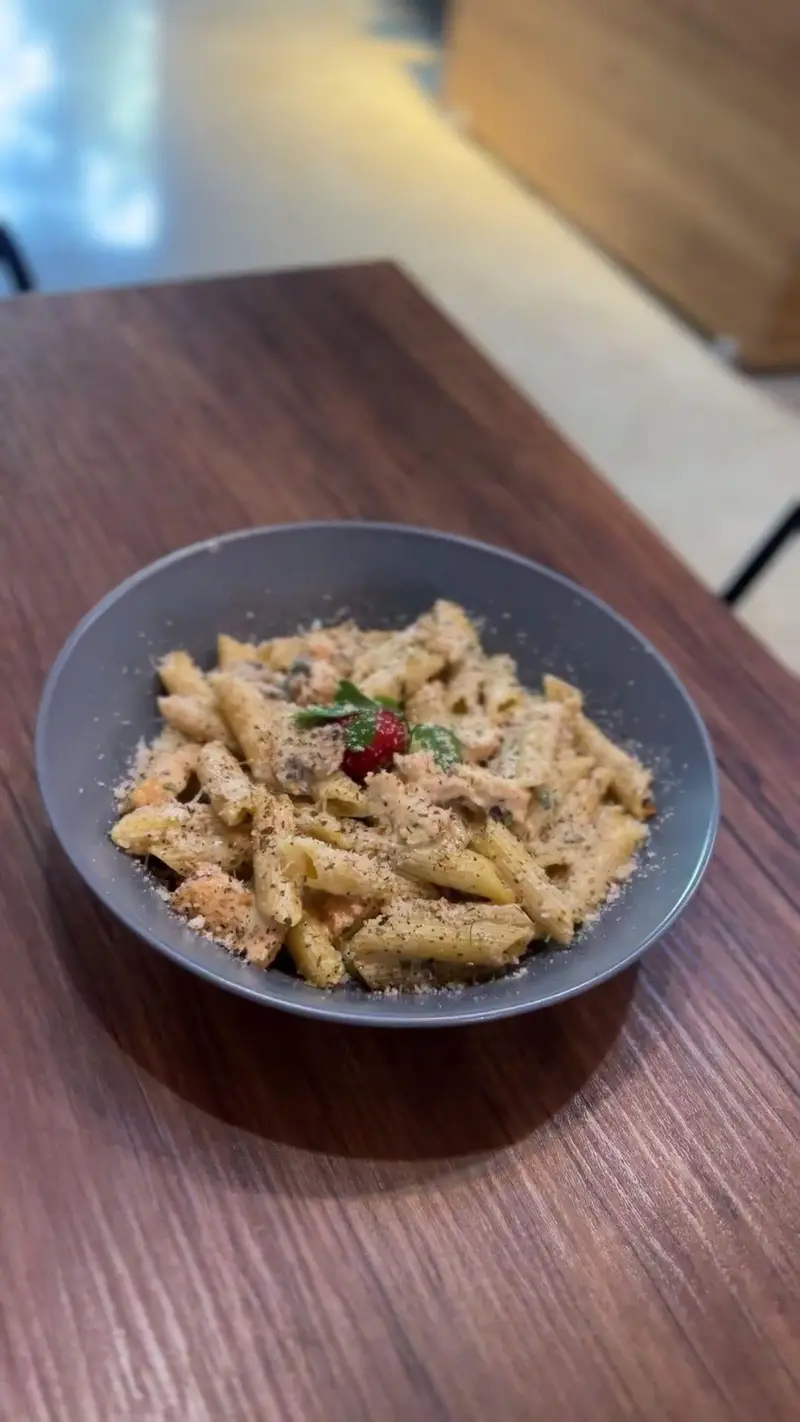 پاستا پنه خامه‌ای و خوشمزه کافه پارس با پنیر پارمزان و سبزیجات معطر، سرو شده روی میز چوبی در فضای دلنشین.