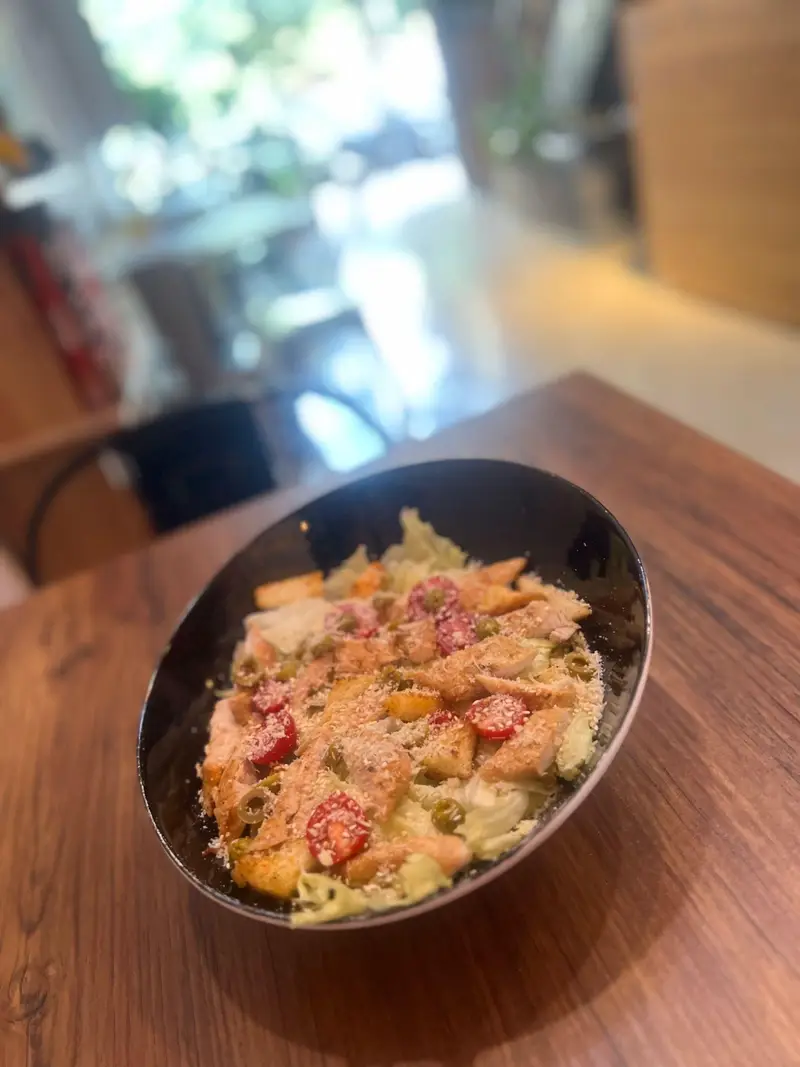 سالاد سزار ویژه کافه پارس با مرغ گریل، زیتون، گوجه گیلاسی و سس مخصوص روی میز چوبی در فضایی دلنشین و آرام.