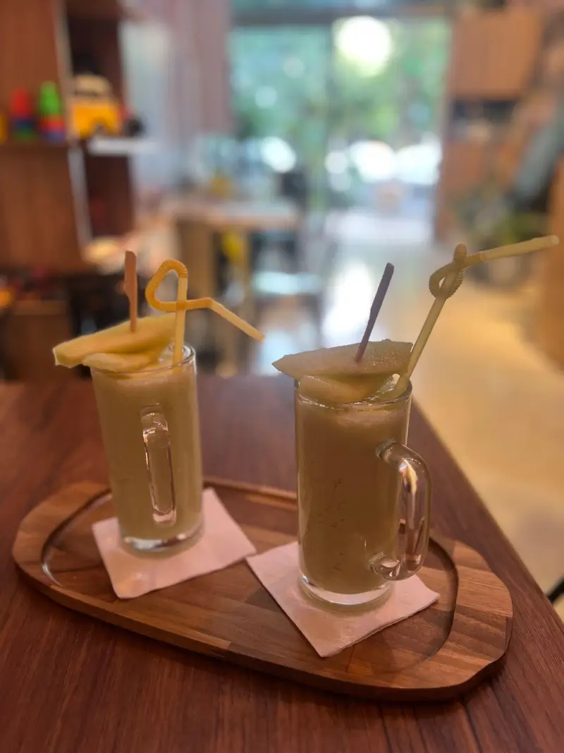 نوشیدنی های خنک و میوه ای کافه پارس، شامل دو لیوان اسموتی تازه با تزئین برش های میوه روی سینی چوبی در فضای دلنشین کافه.