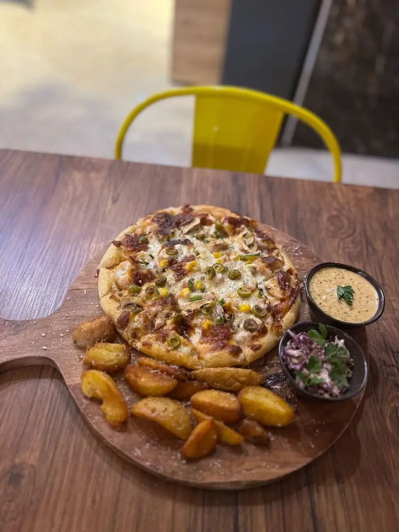 پیتزا سبزیجات و قارچ کافه پارس، همراه با سیب زمینی وِج، سس و سالاد تازه روی تخته چوبی. تجربه طعم‌های جذاب در فضای کافه.