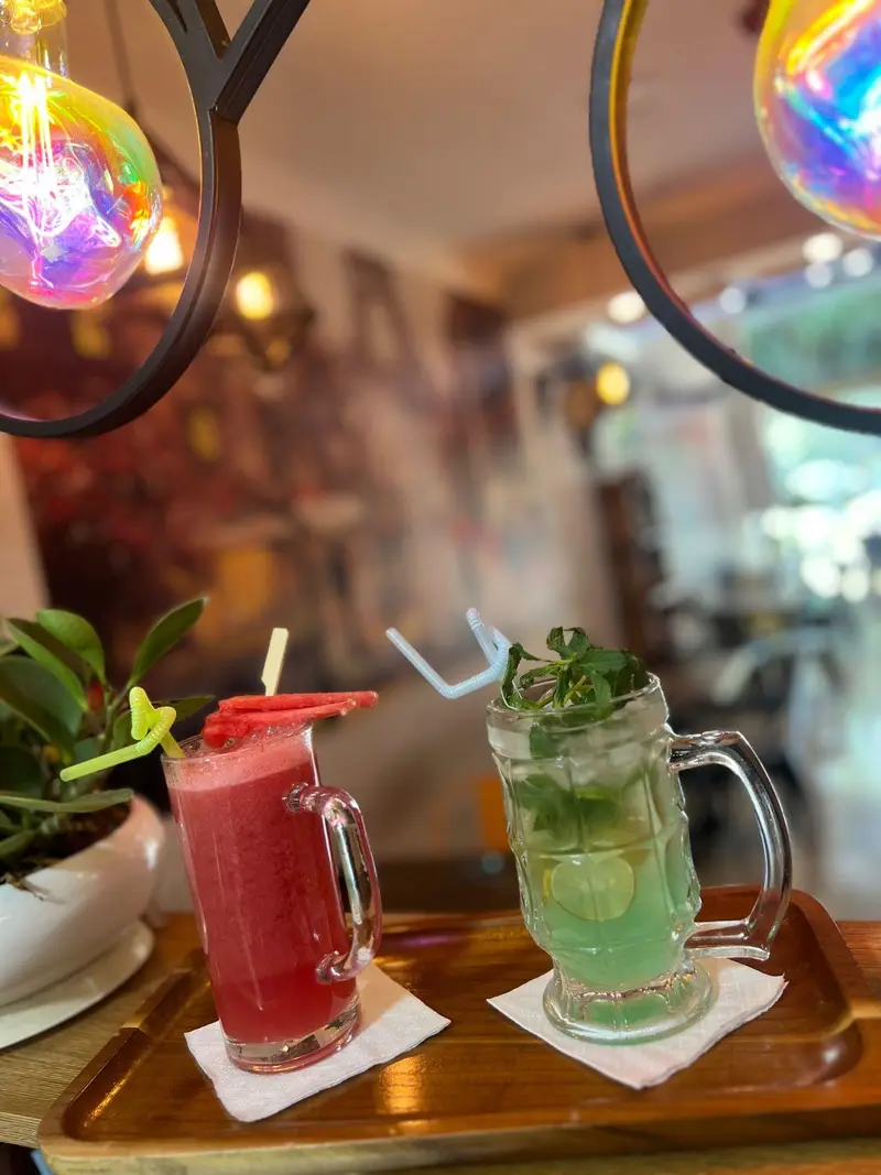 دو نوشیدنی خنک و دلپذیر کافه پارس: آب هندوانه تازه و موهیتو نعناع و لیمو، سرو شده در فضای جذاب و رنگارنگ کافه.