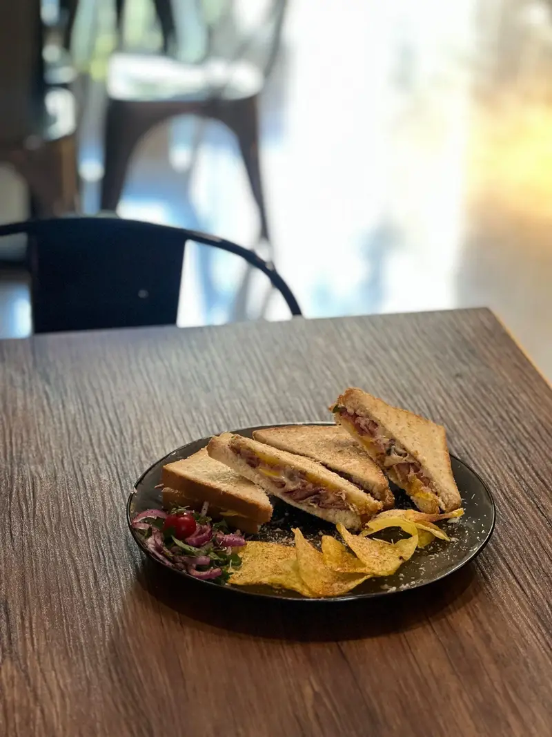 ساندویچ‌های چند تکه کافه پارس با مخلفات رنگارنگ از جمله چیپس و سالاد، آماده برای لذت بردن از یک وعده غذایی لذیذ در فضایی دلنشین.