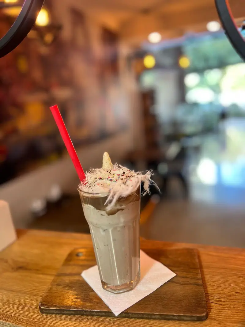 میلک شیک کافه پارس با خامه، پشمک، ترافل رنگی و نی قرمز، دسری خاص و جذاب برای لذت بردن در فضای گرم کافه پارس.