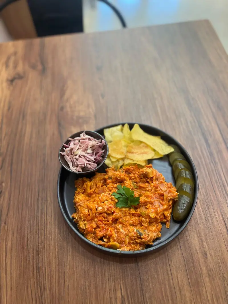 املت ویژه کافه پارس با سس گوجه فرنگی، چیپس، خیارشور و سالاد کلم قرمز روی میز چوبی. صبحانه‌ای لذیذ در کافه پارس.