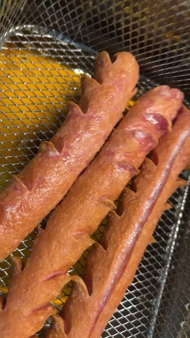 هات داگ‌های تازه و خوشمزه کافه پارس با برش‌های جذاب، در حال سرخ شدن در روغن داغ برای سرو به مشتریان.