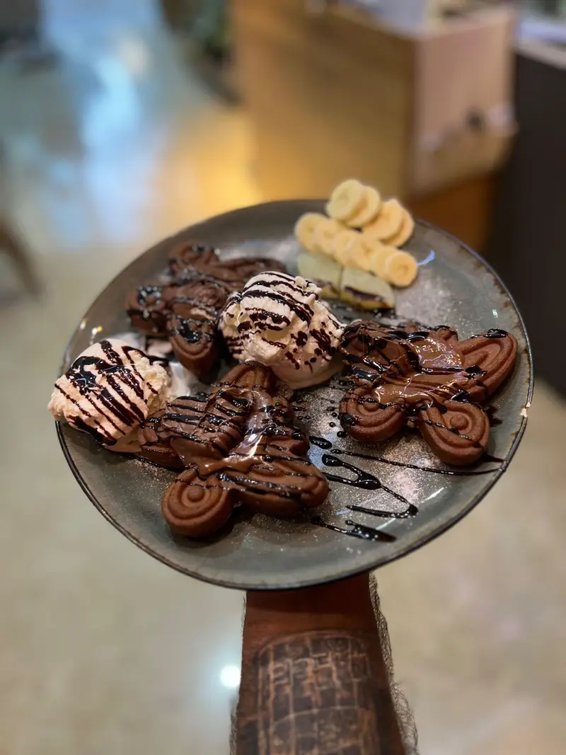 وافل‌های شکلاتی موتورسیکلت کافه پارس، سرو شده با خامه فرم گرفته، سس شکلات و تکه‌های موز تازه؛ دسری دلپذیر و خاص