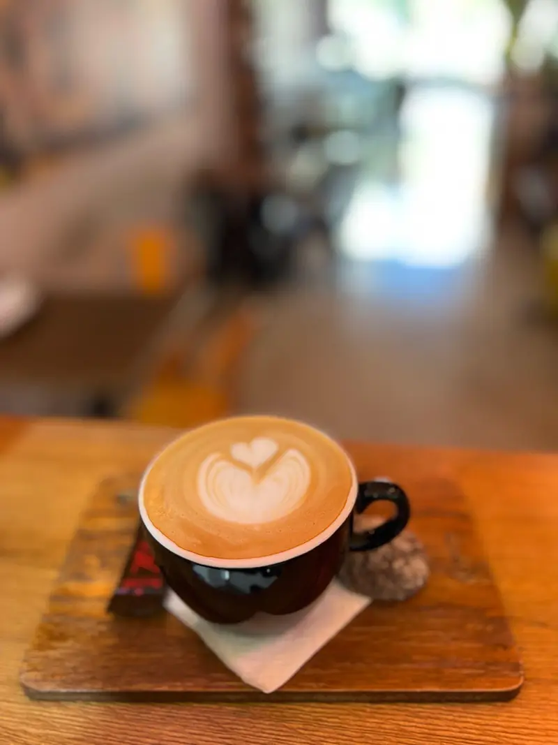 لاته آرت دو قلب زیبا در فنجان مشکی سرو شده روی تخته چوبی در کافه پارس، مکانی دلپذیر برای لذت بردن از قهوه و نوشیدنی‌های گرم در فضایی دنج.