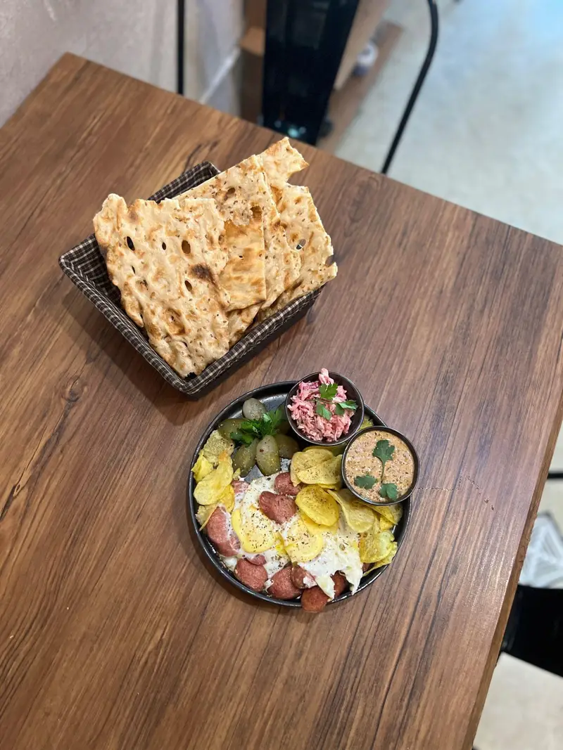 صبحانه کامل و لذیذ کافه پارس: املت سوسیس و تخم مرغ، چیپس، نان محلی، ترشی و سالاد در محیطی دنج و چوبی.