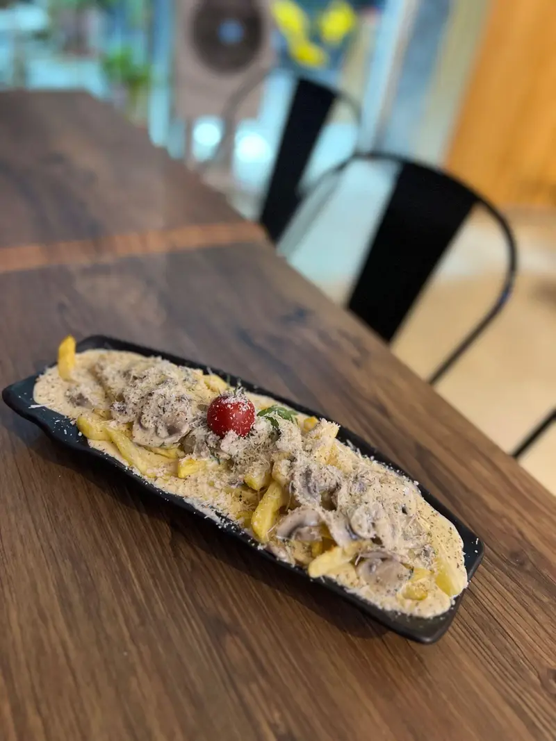 یک بشقاب بزرگ پاستا یا سیب‌زمینی با سس خامه‌ای قارچ و پنیر پارمزان فراوان، تزئین‌شده با گوجه گیلاسی در کافه پارس.