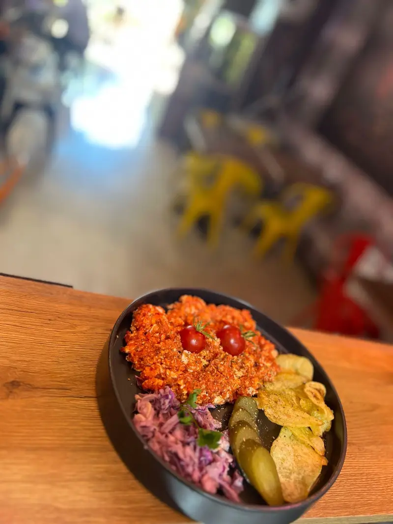 بشقاب صبحانه رنگارنگ و لذیذ در کافه پارس؛ شامل املت، کلم سالاد، خیارشور و چیپس سیب‌زمینی روی میز چوبی با پس‌زمینه کافه.