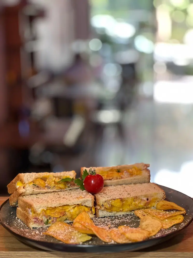 تصویر ساندویچ‌های گریل شده و طلایی کافه پارس، با فیلینگ پنیر و سبزیجات، همراه با چیپس ترد و چاشنی مخصوص. مناسب ناهار یا یک میان‌وعده دلپذیر در کافه پارس.