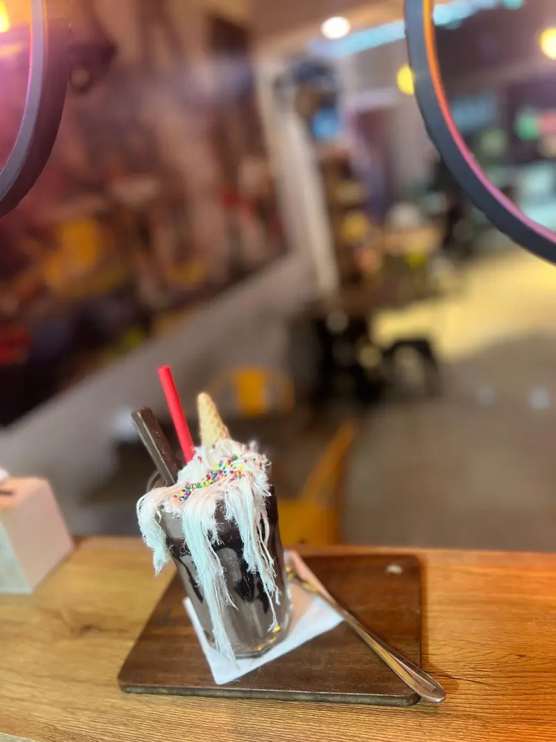 یک لیوان میلک شیک شکلاتی غلیظ و جذاب با خامه سفید، ترافل رنگی و ویفر، میزبان شما در فضای دلنشین کافه پارس.