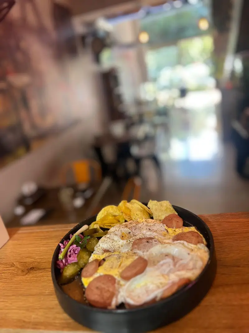 تصویری دلنشین از صبحانه کافه پارس؛ نیمرو با سوسیس، چیپس و ترشیجات، سرو شده در فضای گرم و دوستانه کافه.