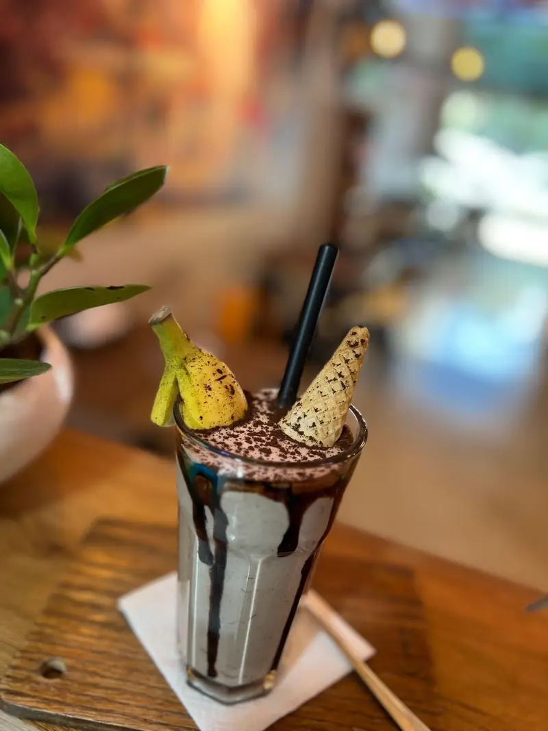 میلک شیک شکلاتی و موز خوشمزه با تزئین پودر کاکائو و ویفر در فضای دنج و دلنشین کافه پارس؛ لذت یک نوشیدنی عالی را تجربه کنید.