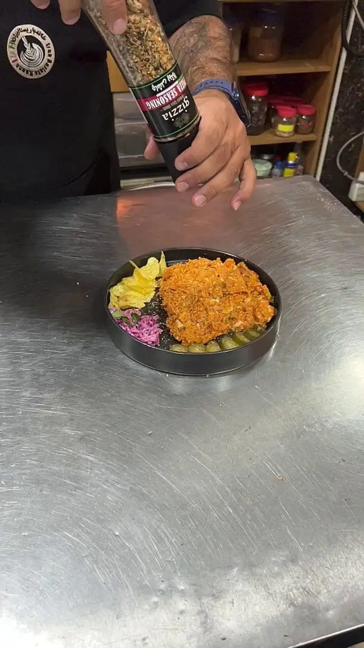 آماده سازی غذای خوشمزه در کافه پارس: سرآشپز چاشنی پیتزا را روی مرغ سوخاری کریسپی، سالاد کلم، چیپس و ترشی می‌پاشد.