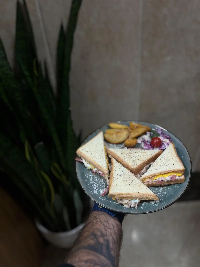 تصویری از ساندویچ‌های کلاب چهار تکه لذیذ کافه پارس در یک بشقاب شیک، همراه با سیب‌زمینی‌های طلایی و سالاد تازه، انتخابی ایده‌آل در منو.