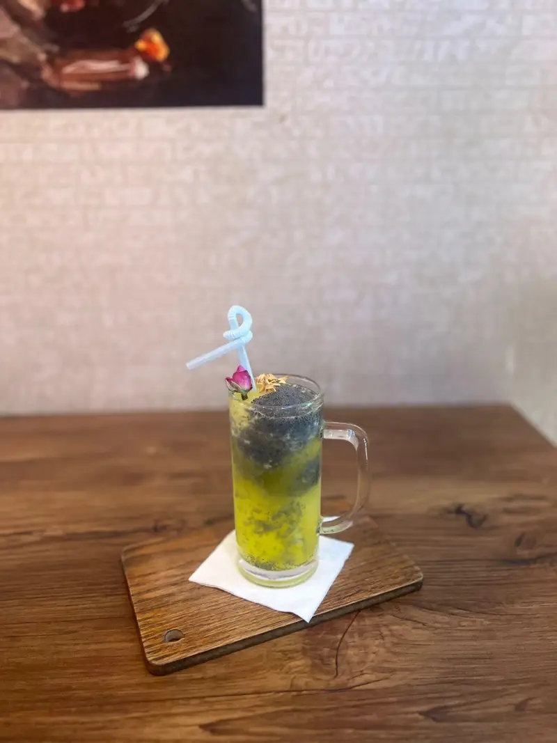 نوشیدنی لایه‌ای و دلچسب کافه پارس با تخم شربتی و گل محمدی، سرو شده روی تخته چوبی، انتخابی عالی برای رفع خستگی و عطش.