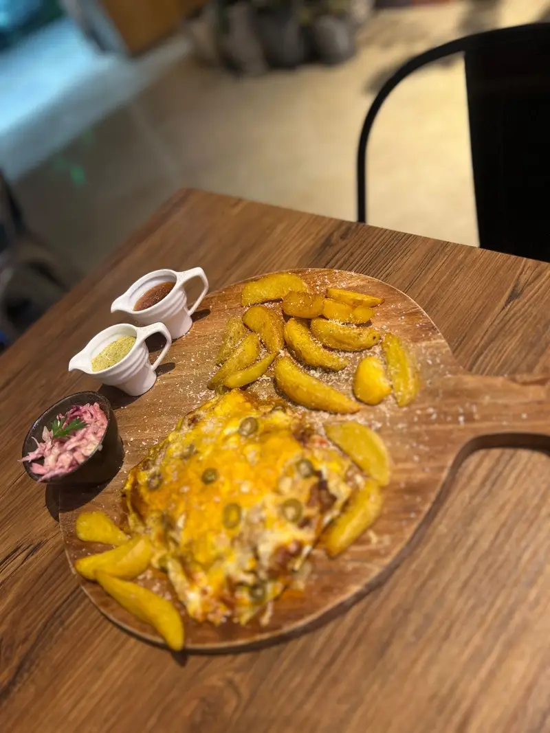 تجربه بی‌نظیر طعم‌ها در کافه پارس: غذای اصلی پنیری با سیب‌زمینی تنوری، سس‌های مخصوص و سالاد کلم بنفش بر روی تخته سرو چوبی.