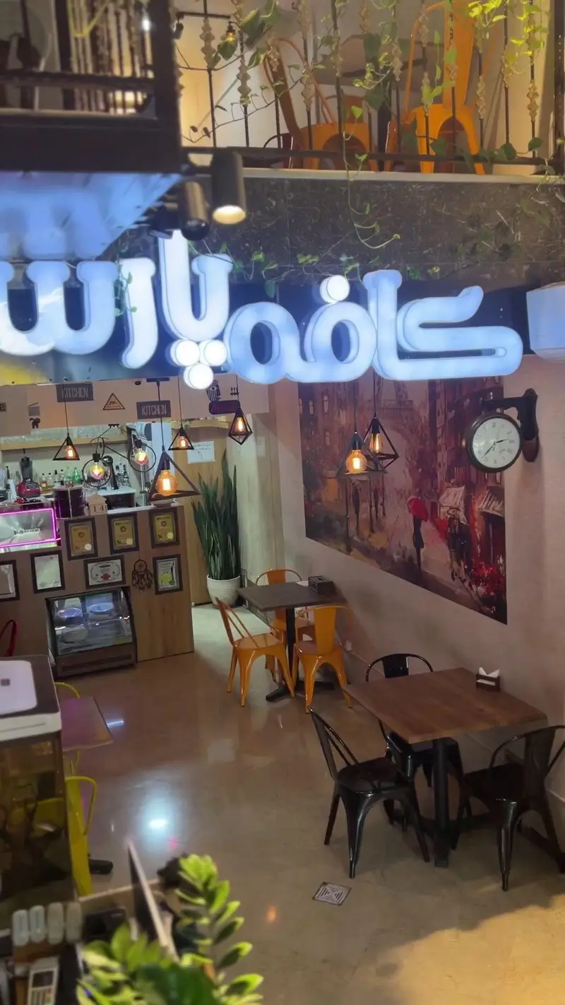 تصویری از فضای داخلی کافه پارس با دکوراسیون جذاب، میز و صندلی‌های راحت، نورپردازی دلنشین و تابلوی نئون نام کافه، نشان‌دهنده محیطی دنج و مدرن.