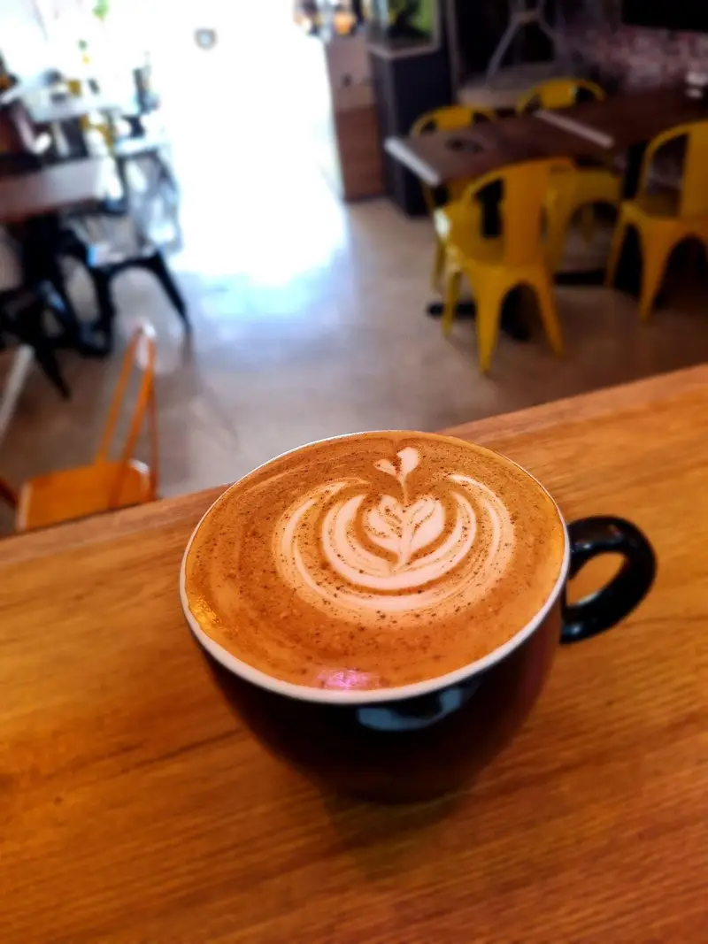 لاته آرت هنرمندانه روی قهوه داغ در فنجان مشکی، نشان‌دهنده کیفیت و زیبایی نوشیدنی‌های کافه پارس در محیطی دلنشین و مدرن.