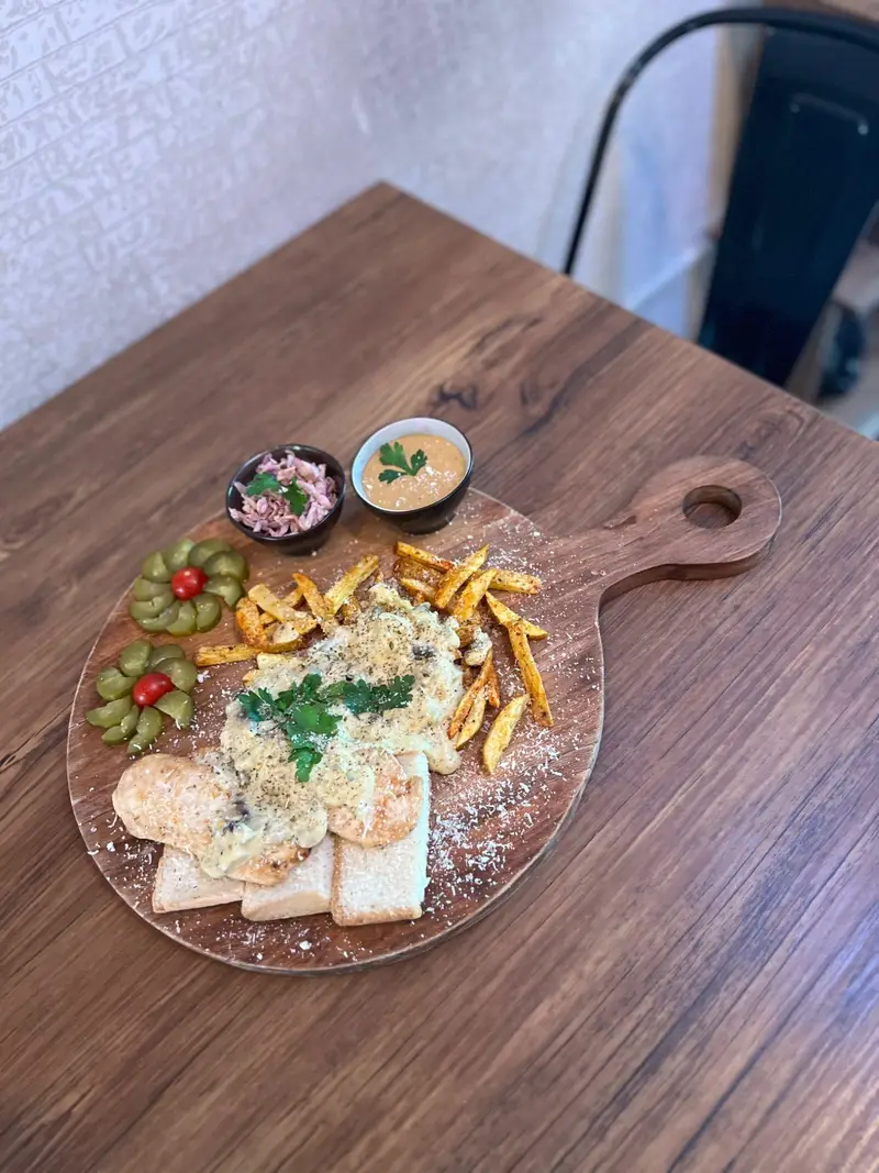 سینی چوبی جذاب کافه پارس شامل فیله مرغ با سس قارچ، سیب‌زمینی سرخ کرده، نان، سالاد کلم و ترشی‌های تزئینی.